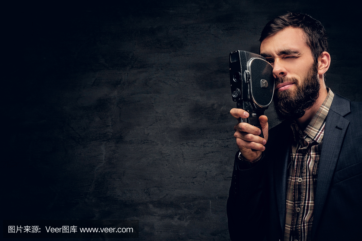 一名身穿西装、蓄着胡须的男子手持老式8毫米摄像机。